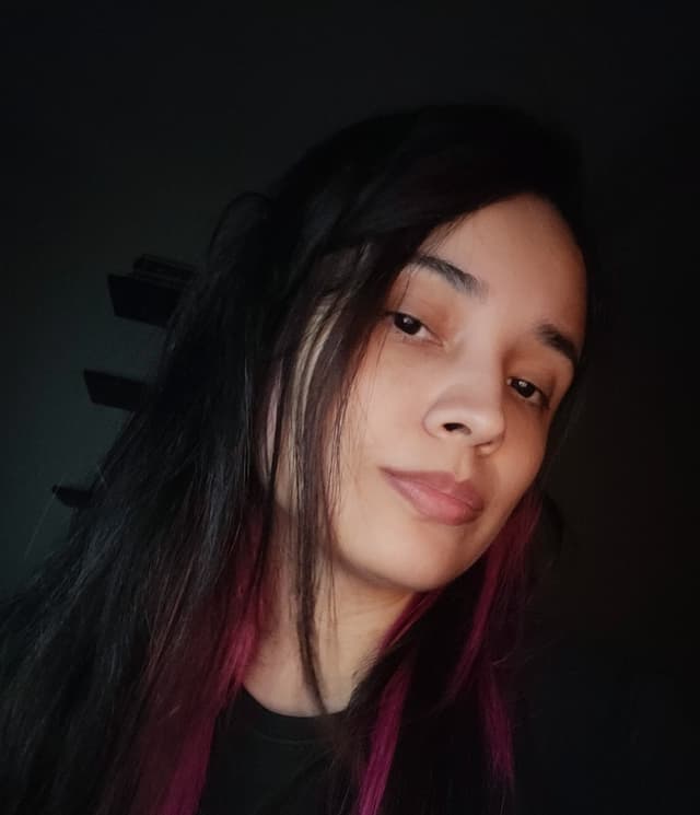 Mulher jovem com cabelo longo e escuro, ligeiramente inclinado para a frente. Parece séria e está vestida com uma camiseta de cor escura.